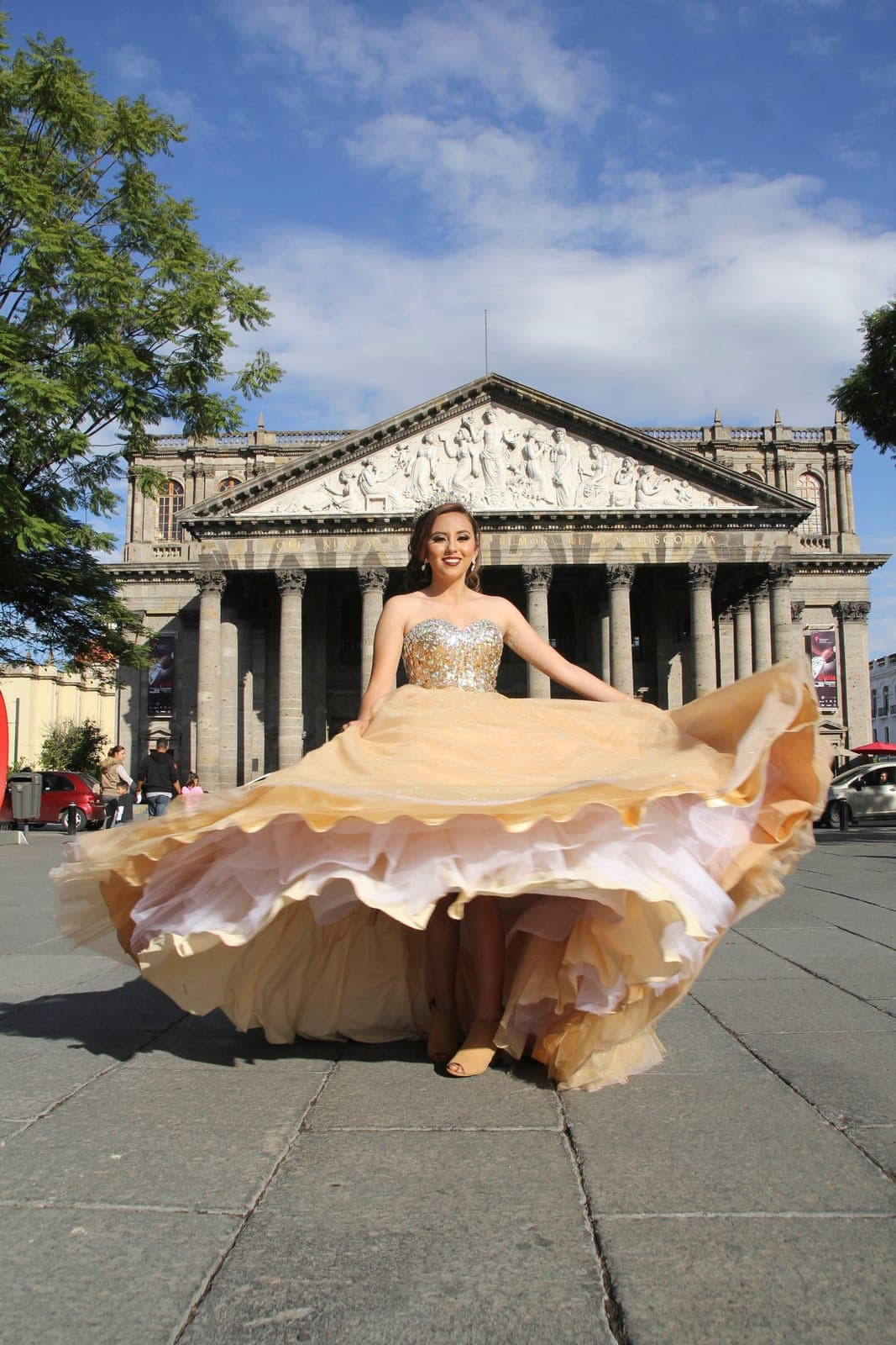 Joven con vestido de gala dorado girando frente a un edificio histórico
