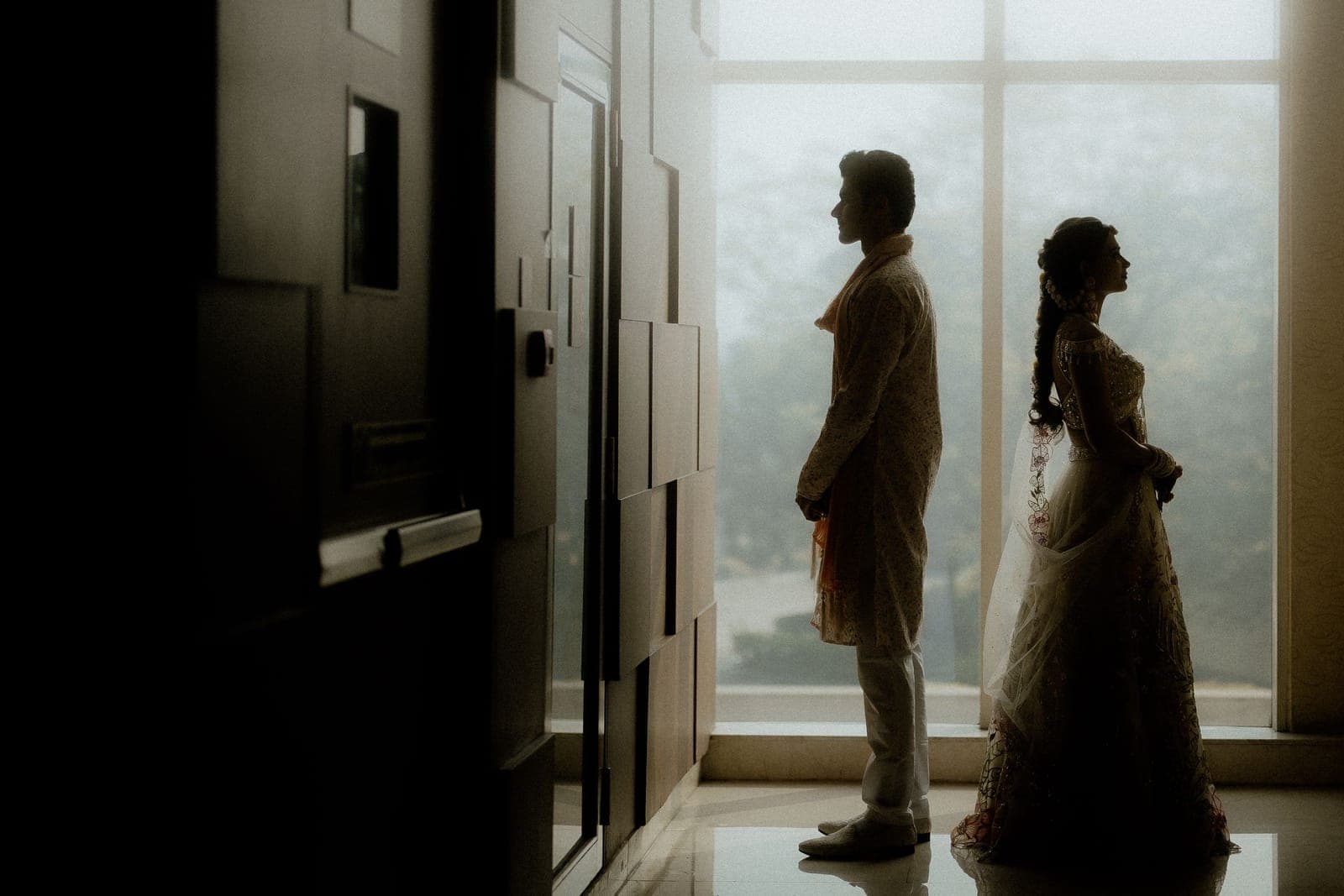 Novios en silueta de pie junto a un ventanal