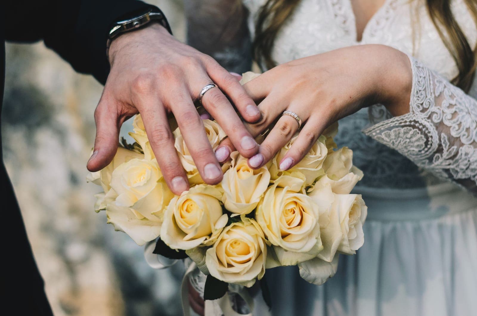 Manos de los novios con sus anillos sobre un ramo de rosas amarillas