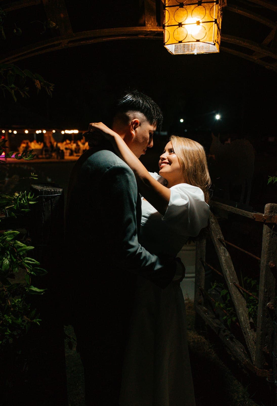 Pareja de novios abrazados de noche bajo una lámpara de luz cálida