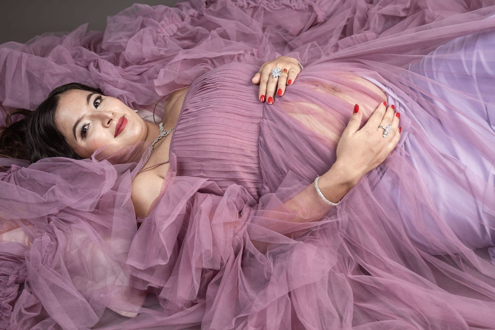 Mujer embarazada recostada sobre un vestido de tul morado